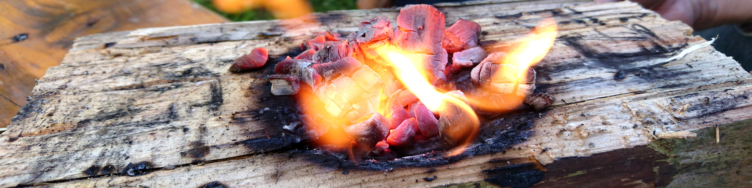 Brennende Glut liegt auf einem Holzklotz und brennt eine kleine Vertiefung als Schüssel ins Holz